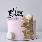A pink frosted birthday cake with gold leaf accents, a black 'Happy Birthday' script topper, and two white macarons , sydney 
