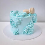 A blue swirling cake with white frosting and decorative elements, macaroon, on top.