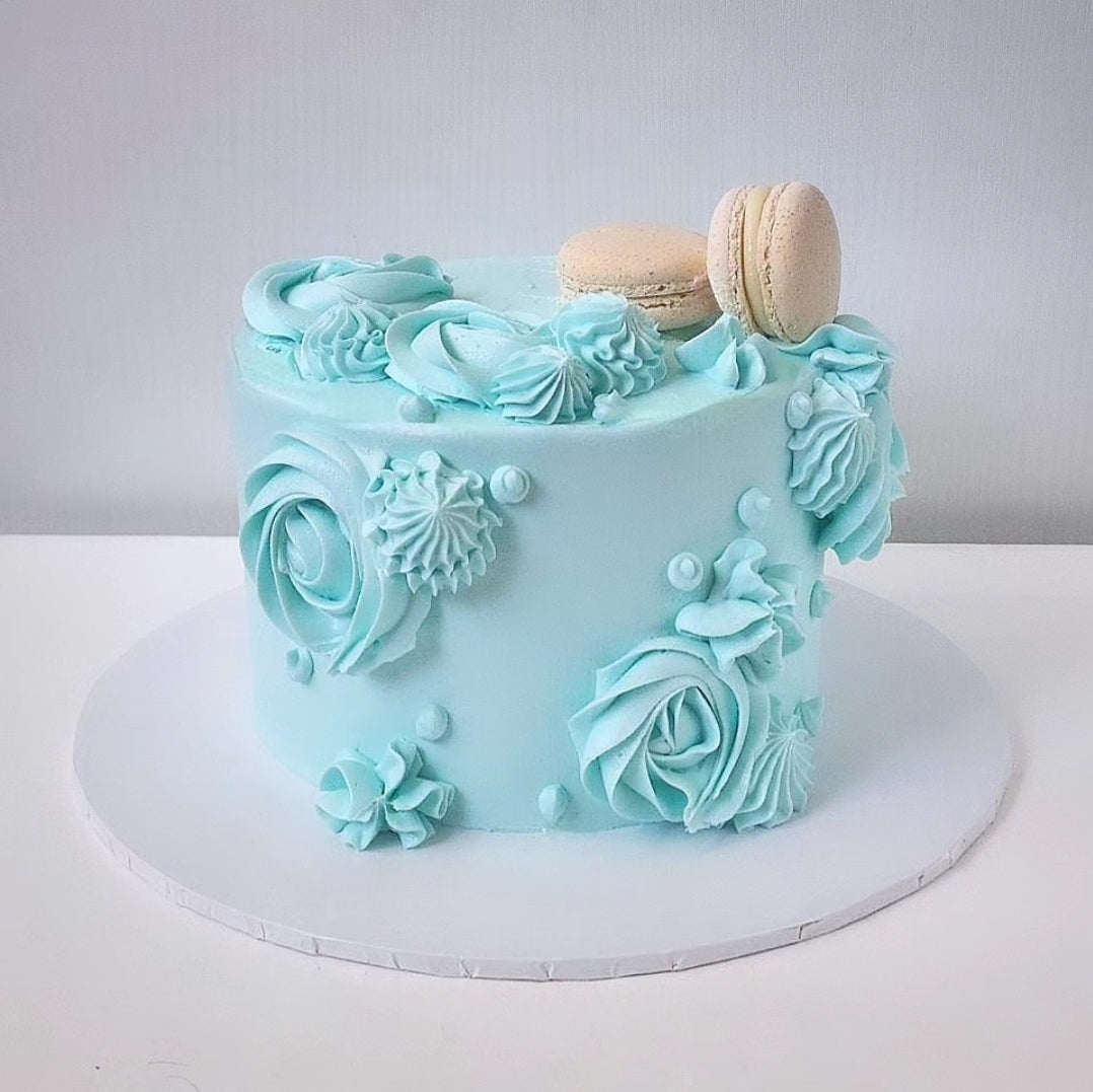 A blue swirling cake with white frosting and decorative elements, macaroon, on top.