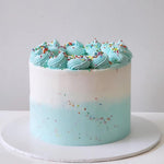 A multi-layered cake with a creamy blue frosting and rainbow sprinkles on top, placed on a white round cake stand.