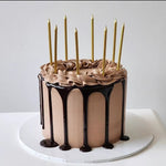 A chocolate cake with golden candles on top, frosted with creamy white chocolate icing.