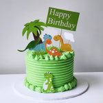 A themed dinosaur cake with a green and white color scheme, featuring cartoonish dinosaur figures and a 'Happy Birthday' sign.