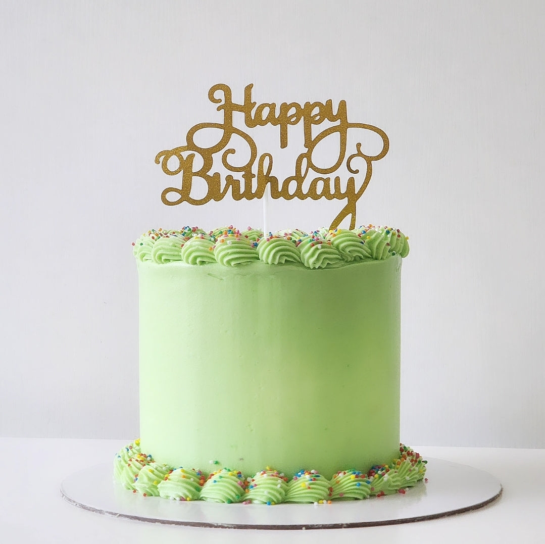 A green party cake with 'Happy Birthday' written in gold letters on top, decorated with a layer of multicolored sprinkles.