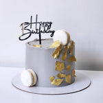 Gray birthday cake with gold decorations and a 'Happy Birthday' topper on a white background