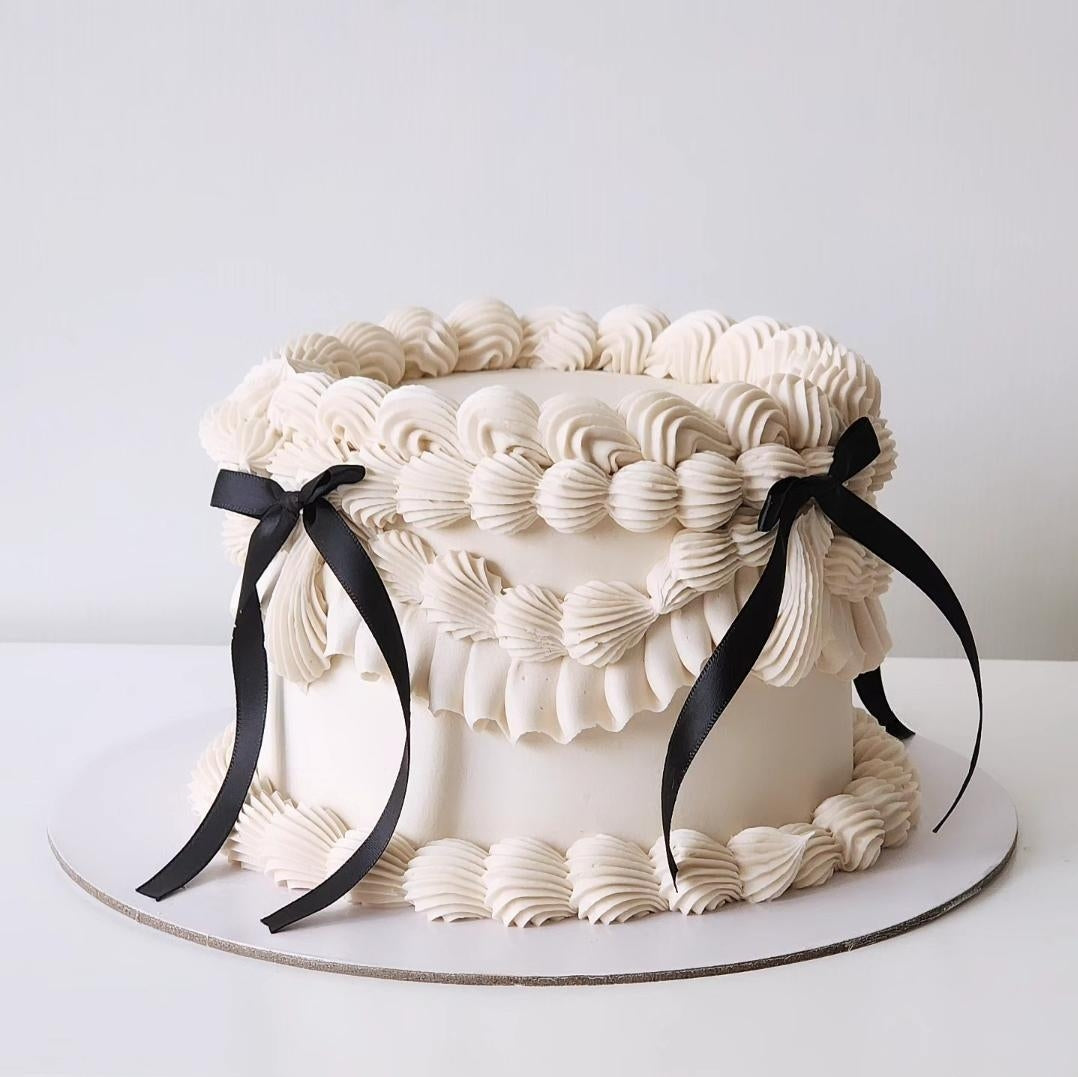A Classic Ivory Cake with white buttercream frosting and decorated with black ribbons.