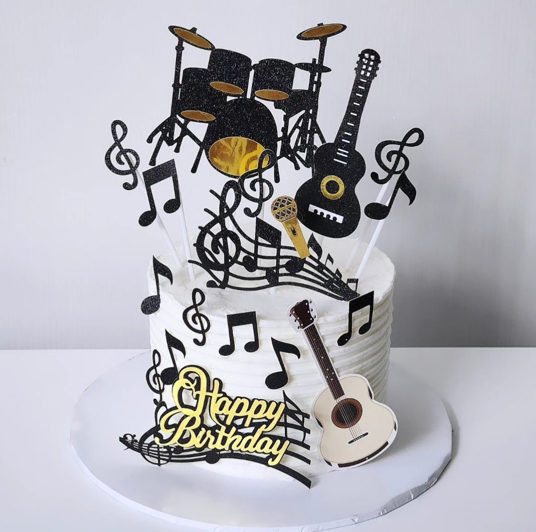 A themed birthday cake decorated with musical notes, a guitar, and a drum set on top, with 'Happy Birthday' text visible.