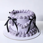 A round cake with a purple buttercream frosting, adorned with a black bow.