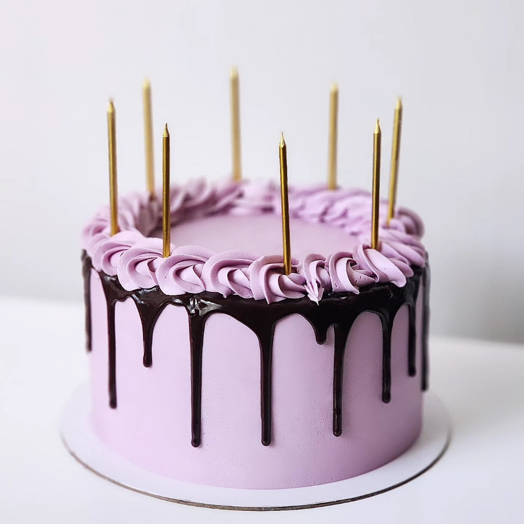 A decorated cake with purple frosting and chocolate drips, featuring golden candles on top.