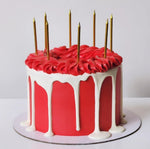 A multi-layered cake with a vibrant red layer and a white layer frosted with chocolate, topped with gold-colored candles.