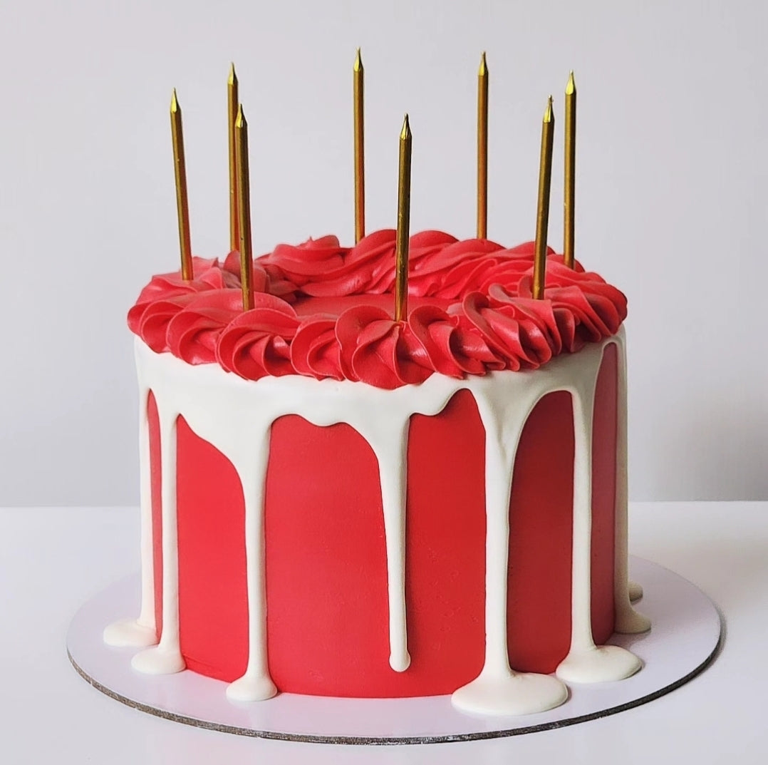 A multi-layered cake with a vibrant red layer and a white layer frosted with chocolate, topped with gold-colored candles.