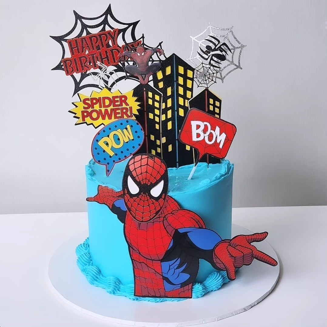 A themed Spider birthday cake with a Spider character motif, layered with a blue and red color scheme, decorated with comic book-style elements and a cityscape backdrop.