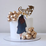 Graduation-themed cake with gold balloons and a 'Congrats Grad' topper on a white background