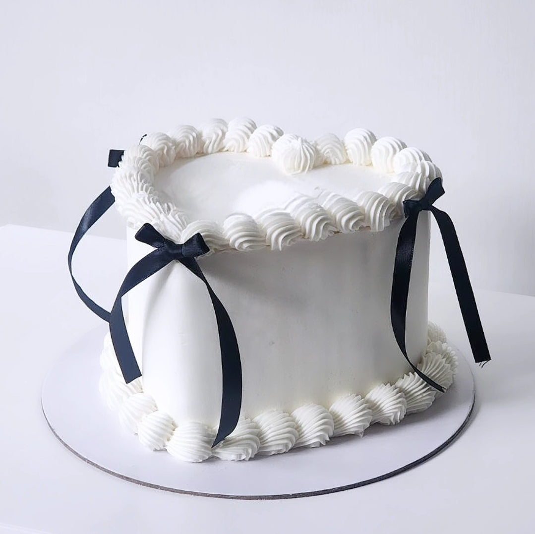 White cake with decorative frosting and black ribbon on a heart shape cake