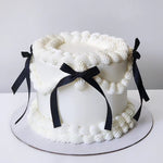 A luxurious multi-layered cake with creamy vanilla buttercream frosting and decorated with black ribbons.