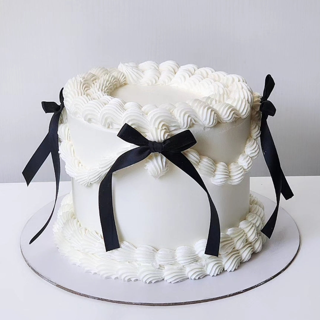 A luxurious multi-layered cake with creamy vanilla buttercream frosting and decorated with black ribbons.