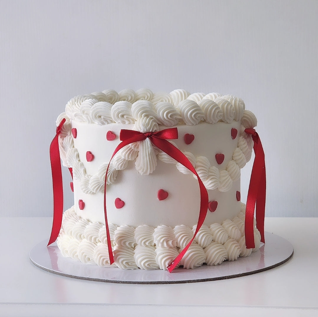 White cake with red ribbons and heart decorations on a white background