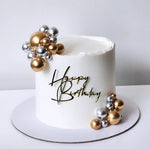 White birthday cake with gold and silver decorations and 'Happy Birthday' text on a white background