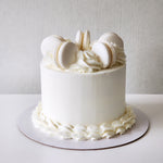 A white, frosted cake with vanilla macarons on top