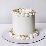 A decorated cake with white frosting and multicolored sprinkles on top, placed on a white cake stand.
