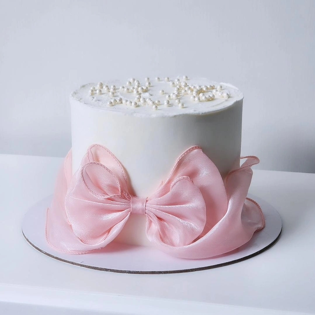 White cake with a pink bow and pearl decorations 