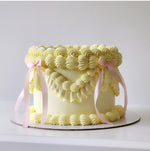 A frosted cake with yellow buttercream icing and decorative pink ribbons.