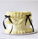 A frosted cake with white icing and black ribbons on top, presented on a white surface.