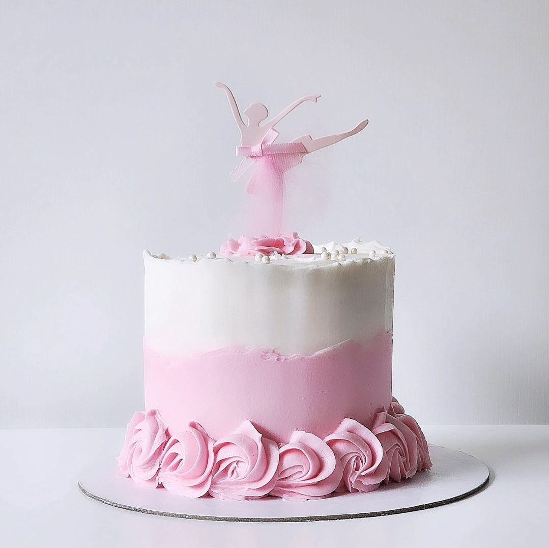 A decorative cake with white and pink layers and a pink ballet dancer figurine on top