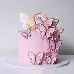 A pink Butterfly Cake decorated with golden butterflies, on a white plate against a grey background.
