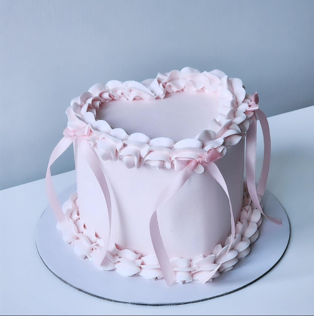 A round cake with pink and white decorative elements on the frosting, a heart cake for a celebration.