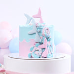 A decorative cake with a mermaid theme, featuring a layer with blue and pink frosting shaped like mermaid tails, and topped with a candy figurine of a mermaid.
