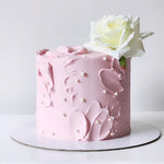 A frosted cake with floral patterns and a white flower decoration on top, presented on a white plate.