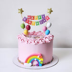 Pink birthday cake with rainbow, stars, and colorful 'Happy Birthday' banner on a white background