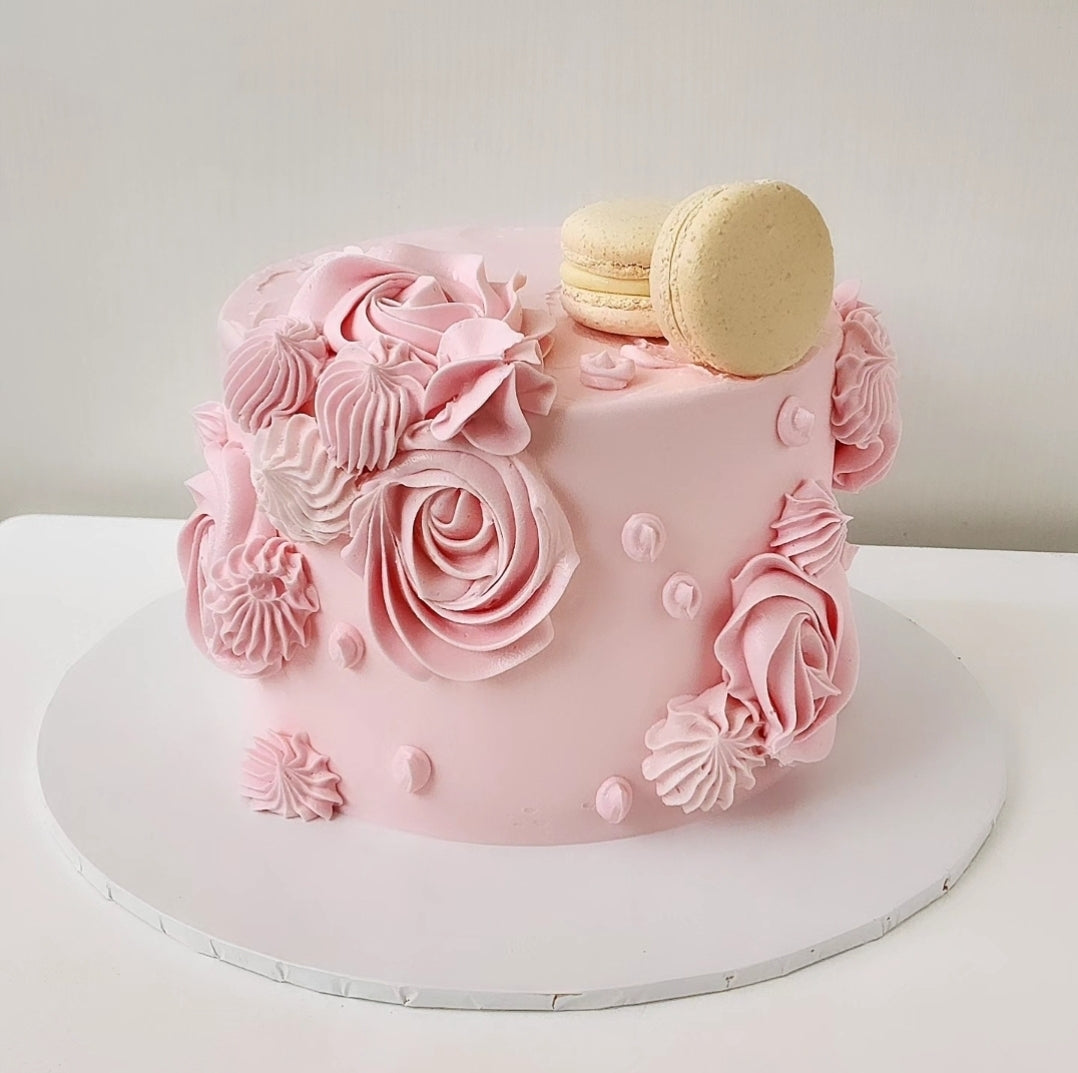 A pink swirled cake decorated with creamy pink frosting and a spiral design, topped with a few macarons.