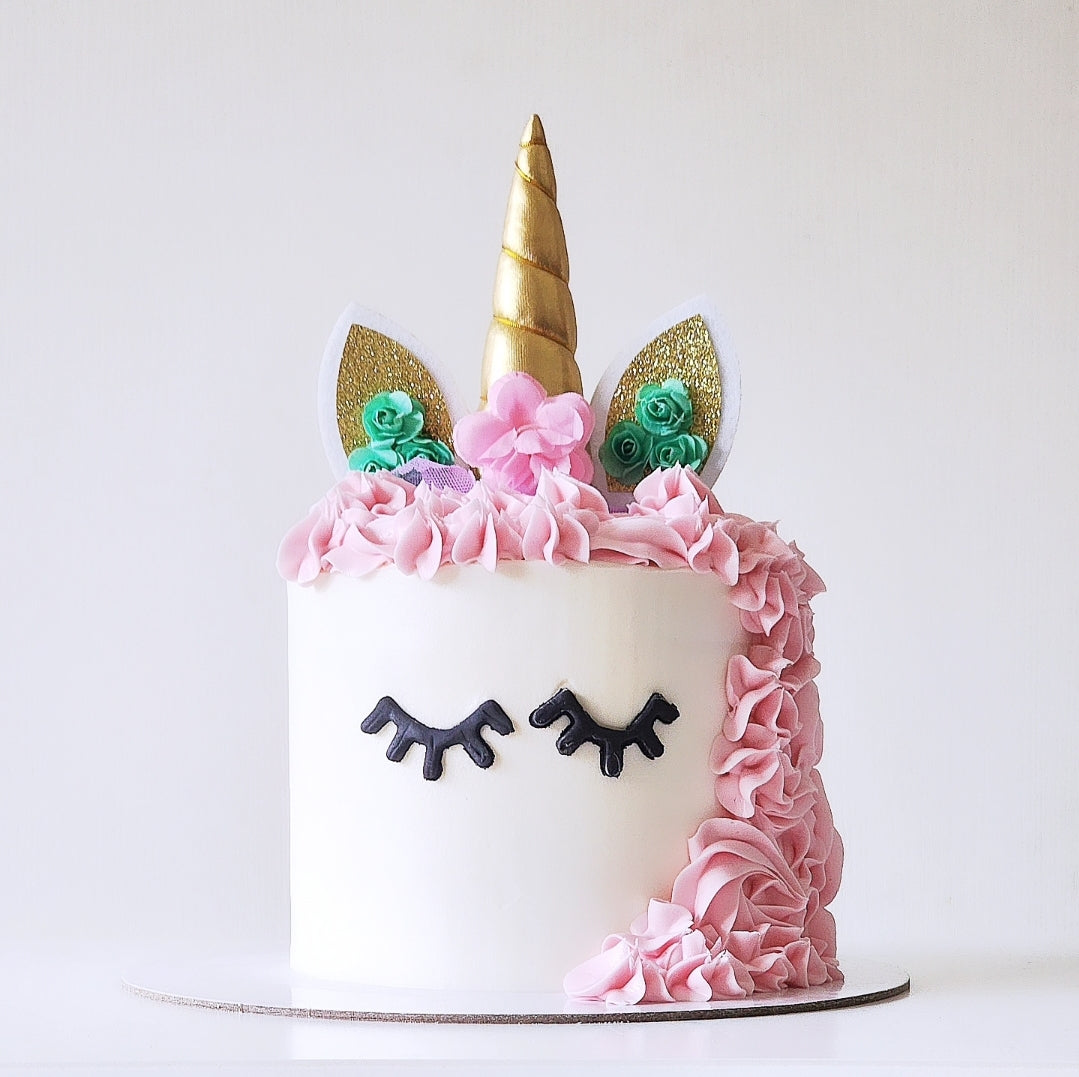 Unicorn-themed cake with decorations, gold horn, and green ears on a white background