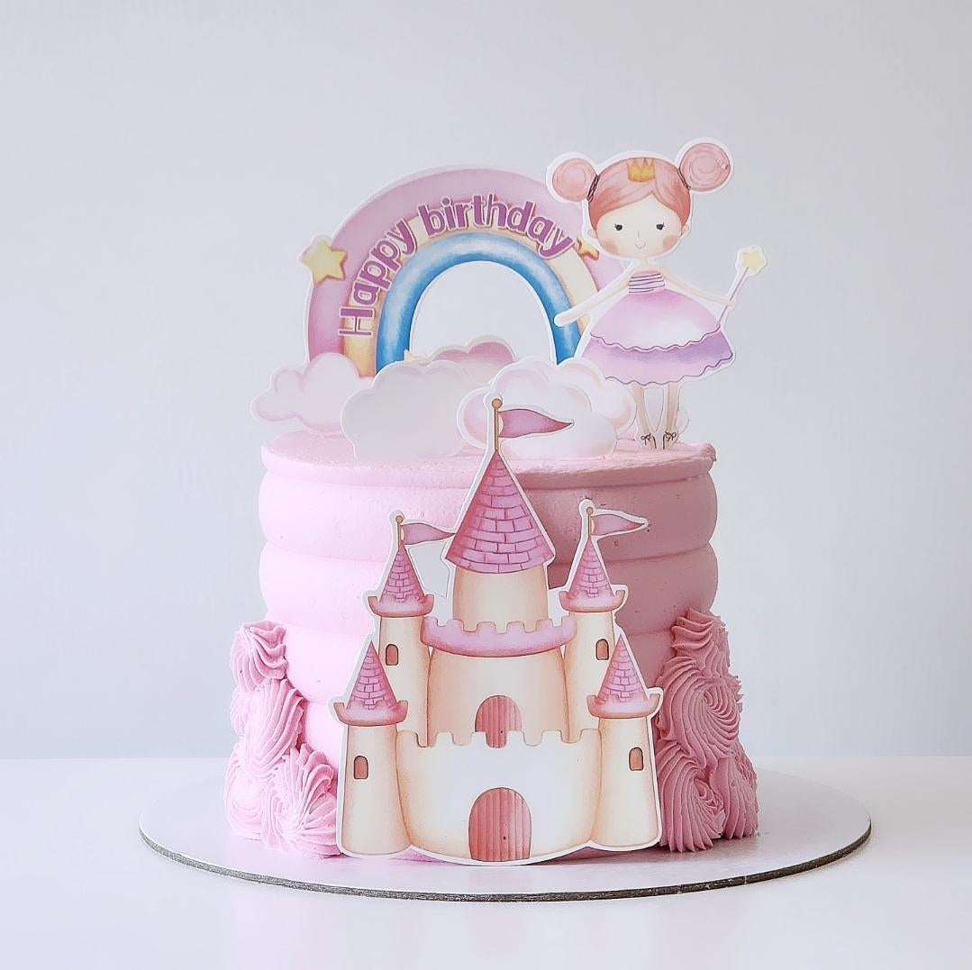 Pink castle cake with fairy and rainbow decoration on a white background