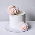 A decorated cake with artificial pink roses on top, placed on a white surface.