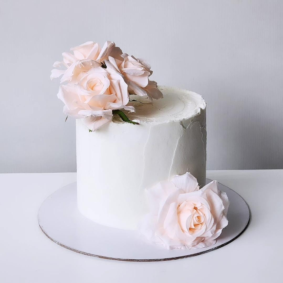 A decorated cake with artificial pink roses on top, placed on a white surface.