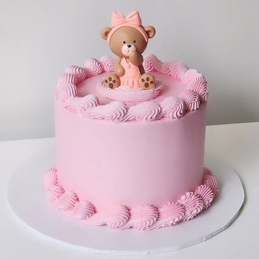 A pink teddy-themed cake, surrounded by pink buttercream decorations 